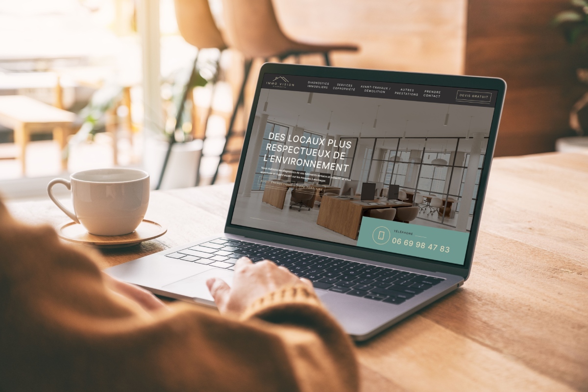 Personne consultant le site IMMO VISION sur un ordinateur portable au café